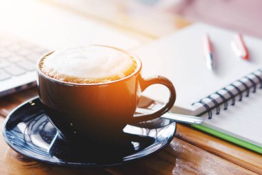 Dizüstü bilgisayar, fincan kahve, not defteri ve kalem ahşap masa üzerinde açılan