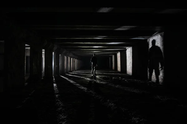 Shilouette and shadow of human underground explorer in abandoned dark tunnel.