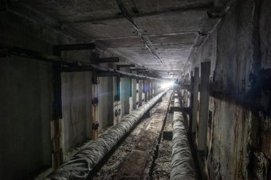 Boruları ve kabloları olan yeraltı beton kullanım tüneli. Sonunda ışık olan yardımcı tünel.