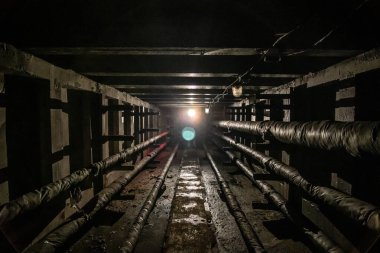 Boruları ve kabloları olan yeraltı beton kullanım tüneli. Sonunda ışık olan yardımcı tünel.
