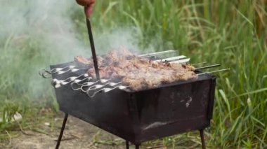 Bir adam şiş kebap pişirirken barbeküde kömür karıştırıyor..