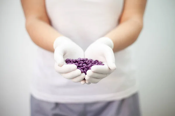 Wax for depilation of purple color. In hands in white gloves. On grey background.
