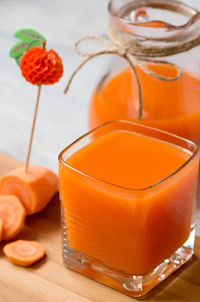 Fresh carrot juice in glass stands on the table . Glass pitcher of juice.