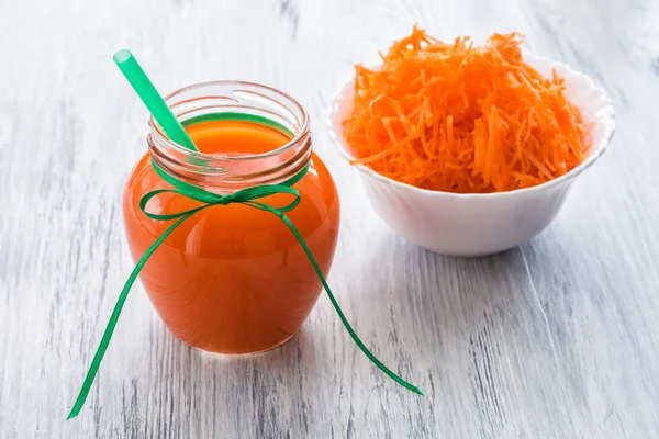 Fresh carrot juice and grated carrots on a plate. Carrot juice on a white wooden table.