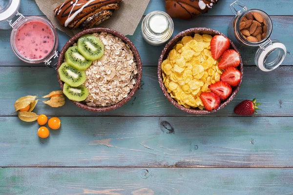 Corn flakes with strawberries and muesli with kiwi on a green wooden background. Cereals,, milk, nuts, berry mousse, fresh pastry, physalis. Healthy eating. From above, copy space.