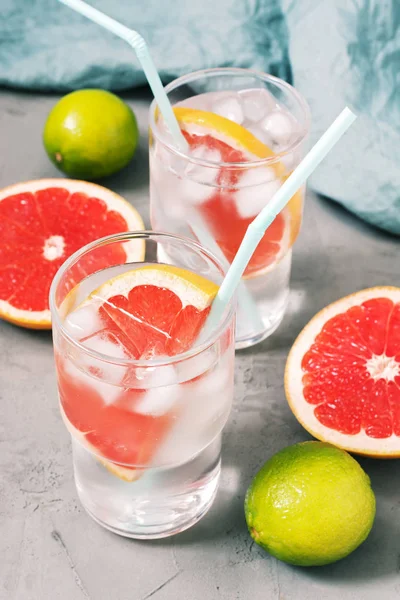 A cooling citrus drink with grapefruit and ice in a glass on a gray concrete background.