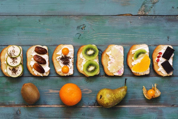 Sweet fruit sandwiches lie in a row on an old wooden green table. Fruit and sandwiches on a rustic table, top view, copy space.