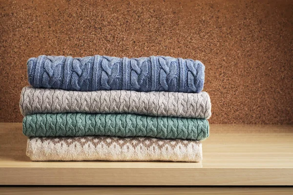 A stack of clothes, colored knitted woolen sweaters on the chest of drawers. Pile winter knitted jacket.