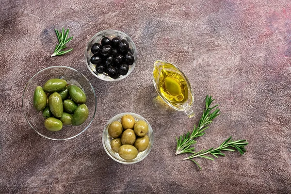 Green and black olives, oil, rosemary herb on a rustic background. Top view, flat lay.