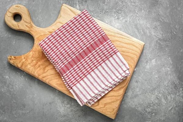 Checkered kitchen towel and wooden cutting board on a gray concrete background. Top view, flat lay.