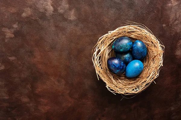Easter. Decorative blue eggs in a nest on a dark brown grunge background. Top view, flat lay, copy space