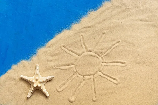Drawn sun on the sea sand and starfish on a blue painted background. Vacation and travel concept. Studio shot
