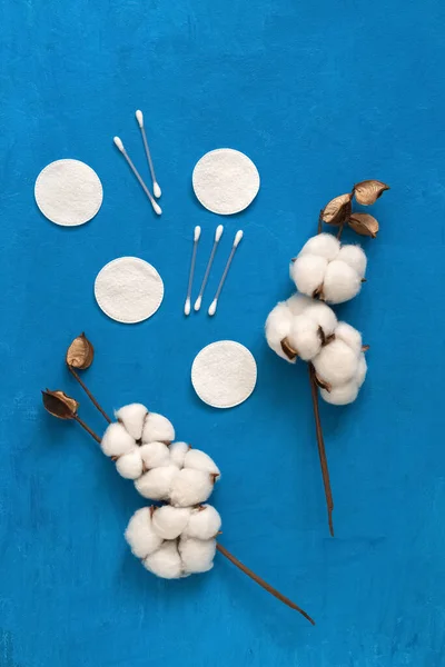 Cosmetic cotton makeup remover. Cotton branches flowers, cotton pads, eared sticks on a blue background. Spa concept. Top view, flat lay