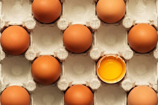 Brown eggs in a carton, one egg is broken. View from above