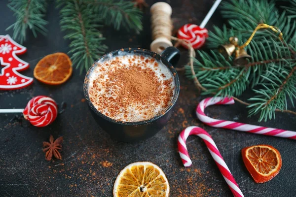 Christmas hot chocolate in a black cup with caramelized oranges, fir branches and candy cane on dark background, Selective focus — Stock Photo, Image