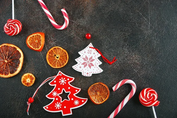 Christmas attributes. Caramelized oranges, fir branches and candy cane on dark background, Selective focus — Stock Photo, Image