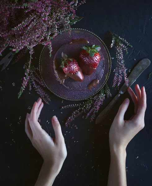Cake with berries, covered with blue-violet glaze and chocolate with flowers, Cosmic cake, Hand Made pastry with woman hands, Dark background, Selective focus