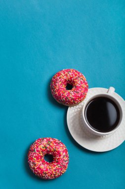Mavi arka planda iki pembe donutlu bir fincan americano.