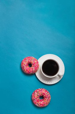 Mavi arka planda iki pembe donutlu bir fincan americano.