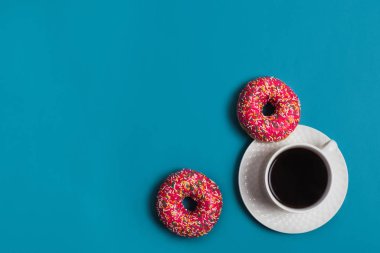 Mavi arka planda iki pembe donutlu bir fincan americano.