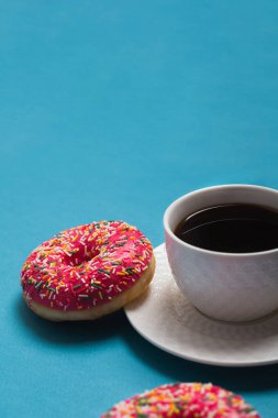 Mavi arka planda iki pembe donutlu bir fincan americano.