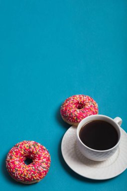 Mavi arka planda iki pembe donutlu bir fincan americano.