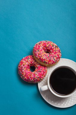 Mavi arka planda iki pembe donutlu bir fincan americano.