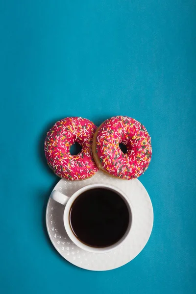 Mavi arka planda iki pembe donutlu bir fincan americano.