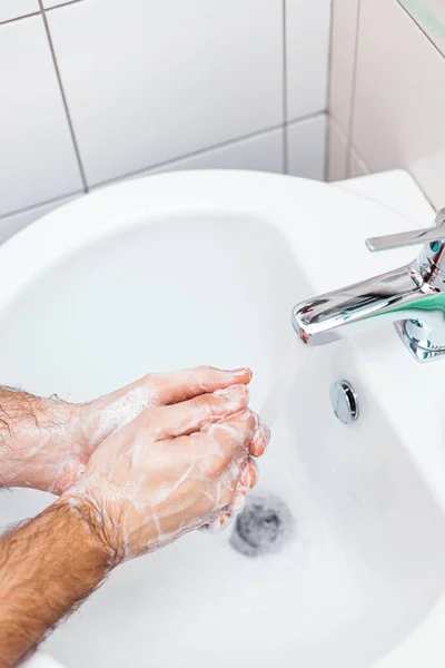 A man washes his hands with soap in the sink