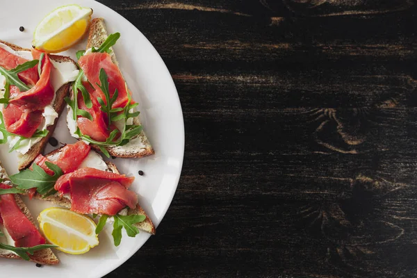 Somon, peynir, roka ve limonlu sandviç siyah bir masada beyaz tabakta.