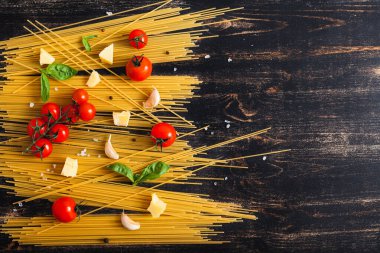 Siyah arka planda çiğ spagetti domates, fesleğen ve peynirli.