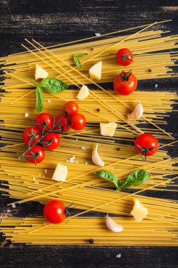 Siyah arka planda çiğ spagetti domates, fesleğen ve peynirli.