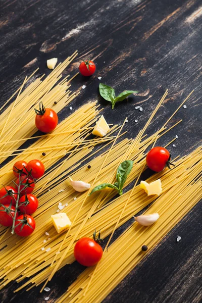 Siyah arka planda çiğ spagetti domates, fesleğen ve peynirli.