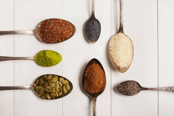 Суперфуды в металлических ложках на белом деревянном фоне. Вид сверху
