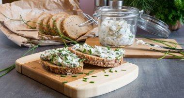 Ev yapımı ekmek, kaymak peyniri, ricotta ve bitkilerle ahşap bir kesim tahtasından. Yeşil otlarla süslenmiş. 