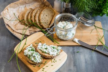 Ev yapımı ekmek, kaymak peyniri, ricotta ve bitkilerle ahşap bir kesim tahtasından. Yeşil otlarla süslenmiş. 