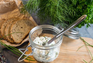 Ev yapımı ekmek, kaymak peyniri, ricotta ve bitkilerle ahşap bir kesim tahtasından. Yeşil otlarla süslenmiş. 