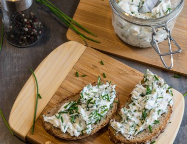 Ev yapımı ekmek, kaymak peyniri, ricotta ve bitkilerle ahşap bir kesim tahtasından. Yeşil otlarla süslenmiş. 