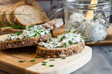 Ev yapımı ekmek, kaymak peyniri, ricotta ve bitkilerle ahşap bir kesim tahtasından. Yeşil otlarla süslenmiş. 