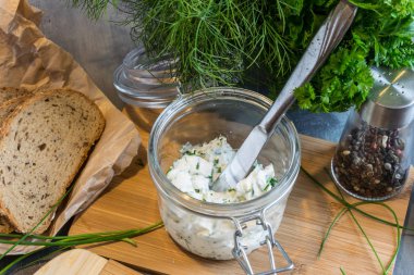 Ev yapımı ekmek, kaymak peyniri, ricotta ve bitkilerle ahşap bir kesim tahtasından. Yeşil otlarla süslenmiş. 