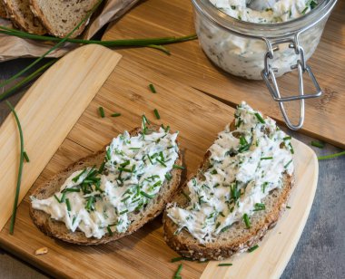 Ev yapımı ekmek, kaymak peyniri, ricotta ve bitkilerle ahşap bir kesim tahtasından. Yeşil otlarla süslenmiş. 