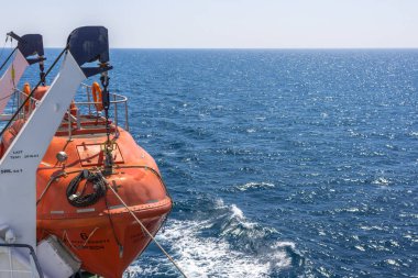 Kilo alan cankurtaran botu. Geminin yan tarafında turuncu tekne var. Deniz taşımacılığı. Açık denizlerde güvenlik. Fırtınaya karşı yedek tekne. Suda güvenlik.