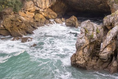 Yüzücünün bakır anıtı. Uçurumdan denize atla. Sahilde bir mağara. Kayalık dağlarda dalgalar. Tehlikeli kayalar. İspanya 'nın doğası. Fırtınalı dalgalar arasında kayalar ve kaldırımlar. Vahşi deniz doğası. 