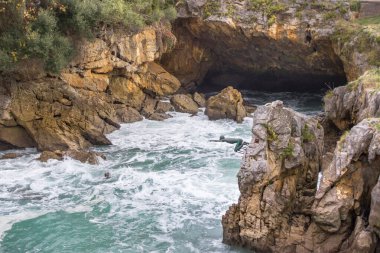 Yüzücünün bakır anıtı. Uçurumdan denize atla. Sahilde bir mağara. Kayalık dağlarda dalgalar. Tehlikeli kayalar. İspanya 'nın doğası. Fırtınalı dalgalar arasında kayalar ve kaldırımlar. Vahşi deniz doğası. 