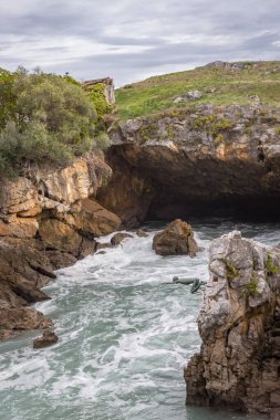 Yüzücünün bakır anıtı. Uçurumdan denize atla. Sahilde bir mağara. Kayalık dağlarda dalgalar. Tehlikeli kayalar. İspanya 'nın doğası. Fırtınalı dalgalar arasında kayalar ve kaldırımlar. Vahşi deniz doğası. 