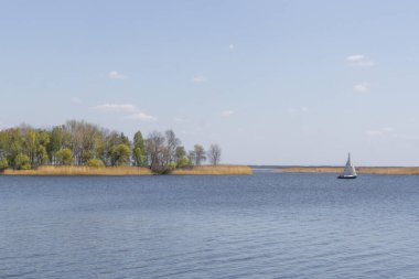 Nehirde ada ve yat. Dinyeper 'da yelkenli bir tekne. Ukrayna 'nın doğası. Resimli bir manzara. Güzel göl manzarası. Baharda kamp yapmak. Suda küçük dalgalanmalar. Rahatlık adacığı.