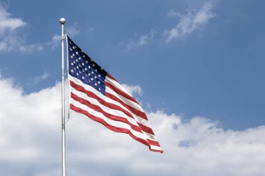 Amerika Birleşik Devletleri bayrağının kırmızı, beyaz ve mavisi, güneşli bir günde bulutlu bir gökyüzü tarafından desteklenen meltemde dalgalanır..