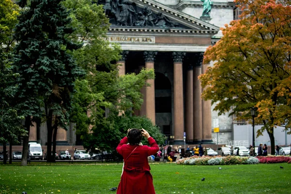 Woman in a red coat photographs the facade of St. Isaac\'s Cathedral in St. Petersburg, Russia