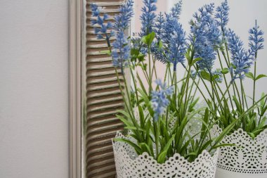 Beyaz bir duvara ve gümüş çerçeveye karşı beyaz bir masada mavi çiçekli beyaz tencere.