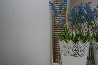 Beyaz bir duvara ve gümüş çerçeveye karşı beyaz bir masada mavi çiçekli beyaz tencere.